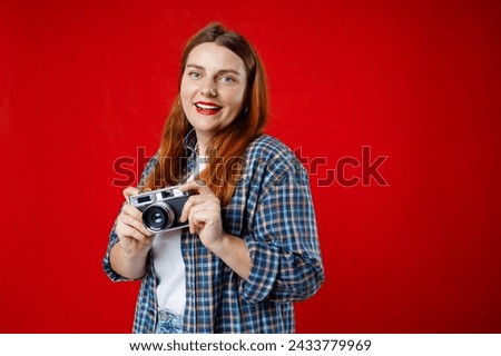 Portrait of a smiling young woman standing with photo camera isolated over red background. Home hobby, lifestyle, travel, people concept