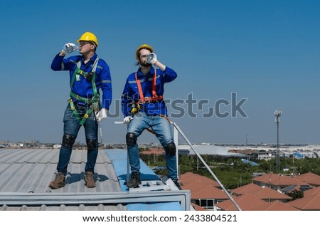 Solar roof technician men drinking water from bottle during break time, roofer men feeling thirsty when working on high roof Royalty-Free Stock Photo #2433804521