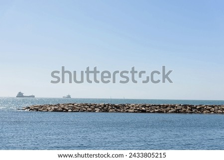 Seascape with a stone pier and lonely ships on the distant horizon on a sunny day