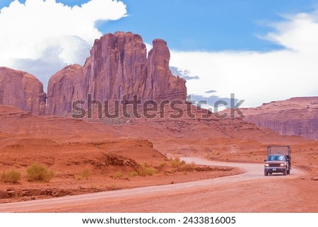 The Monument Valley in Utah–Arizona state with the red earth desert, winding country road and Pick-up truck - USA Royalty-Free Stock Photo #2433816005