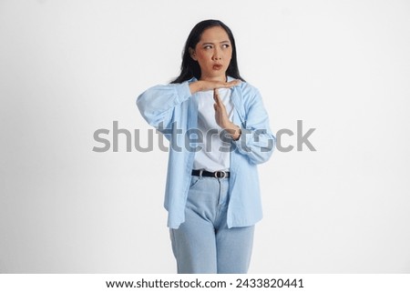 Asian woman wearing casual blue shirt doing time out gesture with hands and serious face, isolated white background