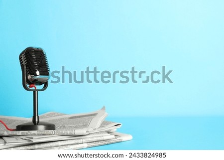 Newspapers and vintage microphone on light blue background, space for text. Journalist's work