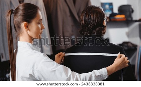 Professional dressmaker taking measurements of businessman in atelier classic menswear. Tailor fitting bespoke suit to handsome man