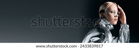 peculiar woman in sci fi glasses and silver attire looking at camera on dark gray backdrop, banner Royalty-Free Stock Photo #2433839817
