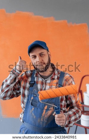 Bearded man holding roller painter smiling doing phone gesture with fingers like talking on the phone. communication concept. Copy space