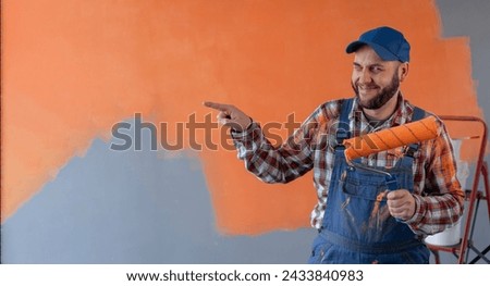Painter or Decorator man holding roller with a smile on his face, pointing with hand finger to the side looking at the camera. Copy space
