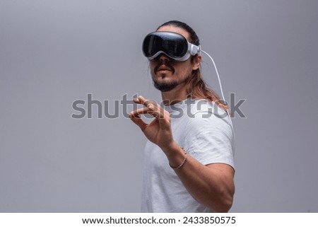 A young man engages with a virtual world using a mixed reality spacial computer headset, symbolizing cutting-edge technology in gaming and immersive digital experiences.  Royalty-Free Stock Photo #2433850575