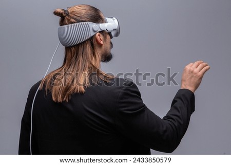 A young man engages with a virtual world using a mixed reality spacial computer headset, symbolizing cutting-edge technology in gaming and immersive digital experiences.  Royalty-Free Stock Photo #2433850579