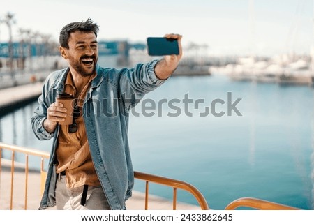 A hipster is making selfies on a pier with his takeaway coffee.