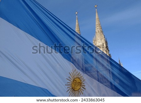 Argentine flag flying. In the background, a religious Gothic temple Royalty-Free Stock Photo #2433863045