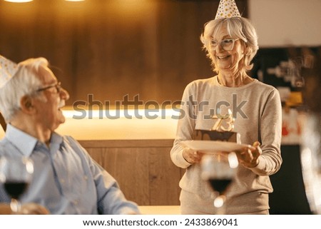 A senior woman is carrying birthday cake and celebrating bday at home.