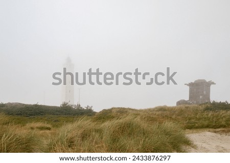 Lighthouse and bunker in the sand dunes on the beach of Blavand in fog, Jutland Denmark Europe Royalty-Free Stock Photo #2433876297