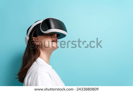Metaverse technology concept. Woman with VR virtual reality goggles on light blue wall background. Futuristic lifestyle. Royalty-Free Stock Photo #2433880809
