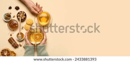 Female hands with glass cups of hot tea with citrus fruit, sugar, spices and cookie on beige background with space for text