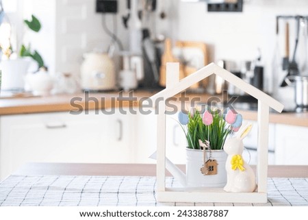 Key and tiny house of cozy home with Easter decor with rabbit and eggs on table of kitchen. Building, design, project, moving to new house, mortgage, insurance, rent and purchase real estate