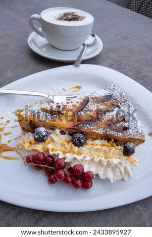 Swiss specialty: Zwetschgenwähe.  Sheet cake usually made from shortcrust pastry with (sweet or savory) toppings.  Here with plums. Decorated with cream and fruit, served with cappuccino  Royalty-Free Stock Photo #2433895927
