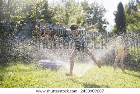 Summer holiday. Happy two kids siblings playing with garden hose and having fun with spray of water in sunny backyard. Summer time. 