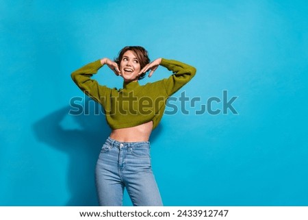 Photo of gorgeous lovely girl wear stylish clothes hands touch face look up empty space offer isolated on cyan color background