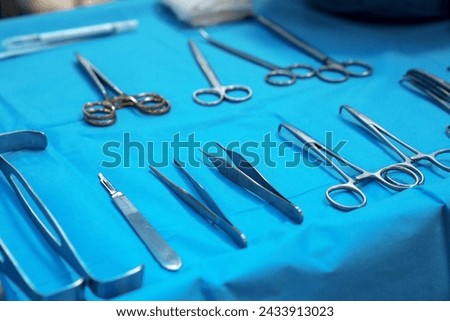 Sterile surgical instruments and tools including scalpels, scissors, forceps and tweezers arranged on a table for a surgery, Sterilized surgical instruments on the blue wrap	 Royalty-Free Stock Photo #2433913023