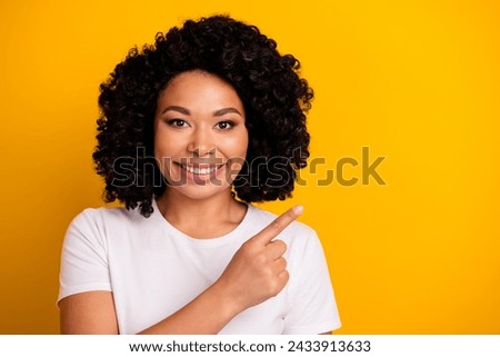 Photo of optimistic woman with perming coiffure dressed white t-shirt indicating at logo empty space isolated on yellow color background