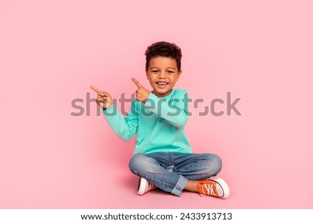 Full size photo of charming small boy sit floor point empty space wear trendy aquamarine outfit isolated on pink color background