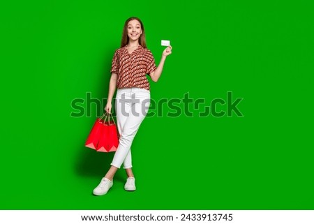 Full size photo of smart beautiful teenager holding shopping bags demonstrate debit card in arm isolated on green color background