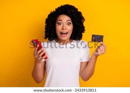 Photo of attractive beautiful impressed woman with chevelure holding smartphone plastic card staring isolated on yellow color background