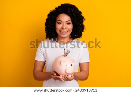 Photo of positive cheerful intelligent woman dressed white t-shirt hold piggy money box in hands isolated on yellow color background