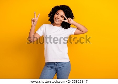 Portrait of good mood gorgeous girl with curly hairstyle wear white t-shirt showing v-sign on eye isolated on yellow color background