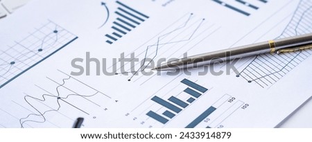 A modern silver pen placed on top of a detailed financial report, showcasing various charts such as bar graphs, line graphs, and pie charts, illustrating market trends and financial data analysis.