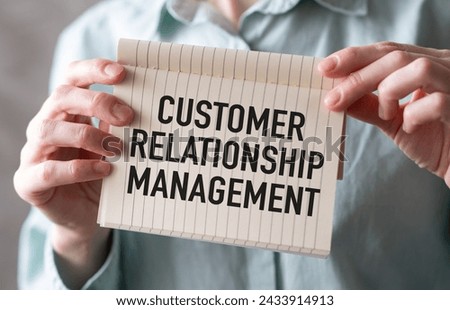 Professional businesswoman with long dark hair holding a sign that reads Customer Relationship Management. Wearing green shirt, serious expression, studio shot on grey background.