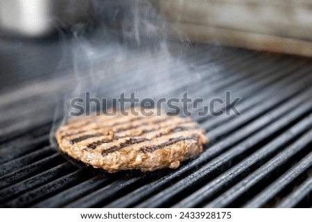 A sizzling burger patty cooks on a grill, smoke rising from its appetizing grill marks