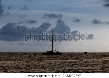 Backlight of boat at sunset beach in Cartagena, Colombia, as people stroll and enjoy the scenery.
