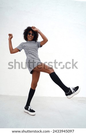 Young woman with afro hairstyle dancing on the white wall. Girl wearing fashionable casual clothes, street style. A lot of copy space.
             