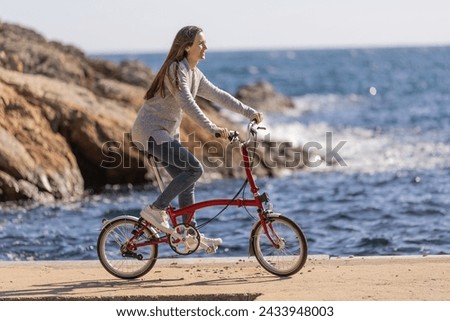 Side view of young woman riding an urban bicycle by the sea Royalty-Free Stock Photo #2433948003