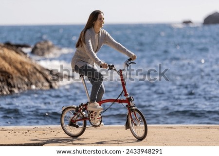 Side view of smiling woman riding an urban bicycle by the sea Royalty-Free Stock Photo #2433948291