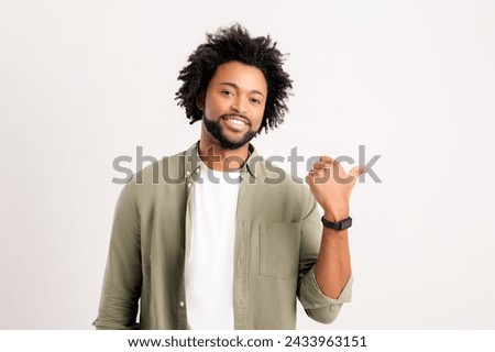 Handsome African-American young man in shirt points aside isolated on white. Friendly well-looking multiracial man paying your attention at copy space, best deal, sale, presenting novelty Royalty-Free Stock Photo #2433963151