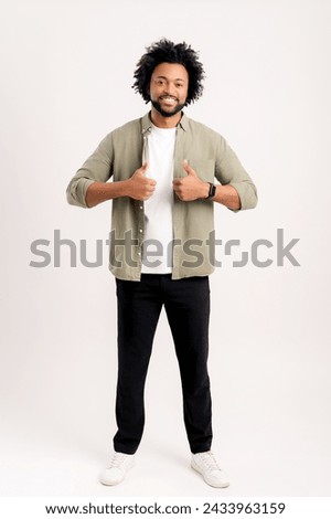 Portrait of man wearing casual style, showing big fingers to camera playfully and smiling, choosing lucky winner. Indoor studio shot isolated on white background
