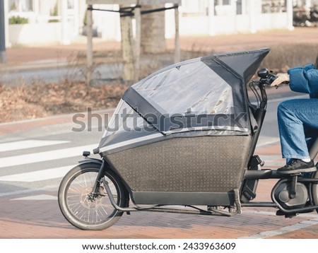 A woman is riding a bike with an attached enclosed trailer on a city street, showcasing modern urban transportation solutions Royalty-Free Stock Photo #2433963609