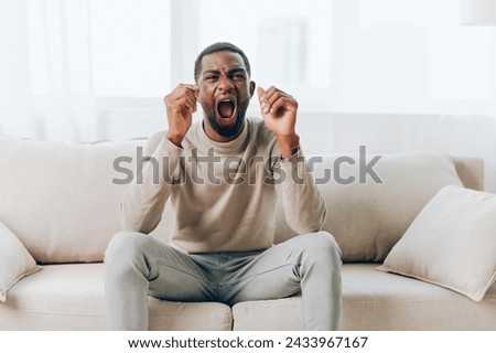 Tired African American man on the couch suffering from a headache at home The stressed and sick individual is alone in his living room, displaying signs of anxiety, depression, and fatigue With a sad