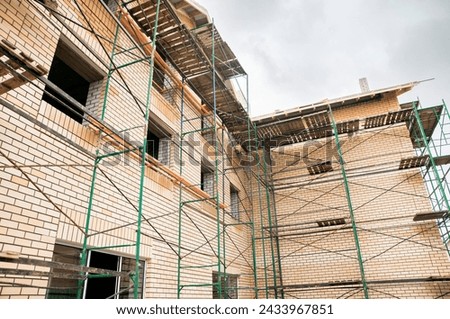 Brick house under construction, three-story cottage in developing with scaffold, elite residential complex, building business Royalty-Free Stock Photo #2433967851