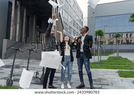 Cheerful multiracial friends having fun together near office and scattering business paper documents over themselves