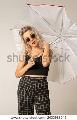 woman WITH WHITE CURLERS with an open umbrella over her head wearing a BLACK suit posing in PHOTO STUDIO