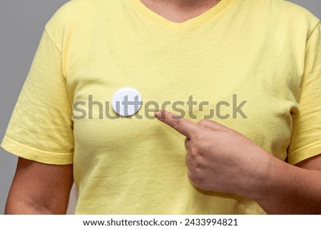 Woman in yellow shirt pointing at a shiny round button. Isolated pin badge mockup Royalty-Free Stock Photo #2433994821