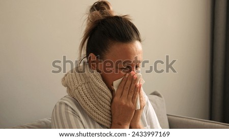 Sick woman wrapped in scarf coughing sneezing battling virus Shows symptoms of virus seeking relief Home care for virus evident in her discomfort Virus symptoms highlight need for rest and recovery Royalty-Free Stock Photo #2433997169