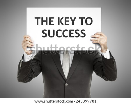 A business man holding a paper in front of his face with the message the key to success