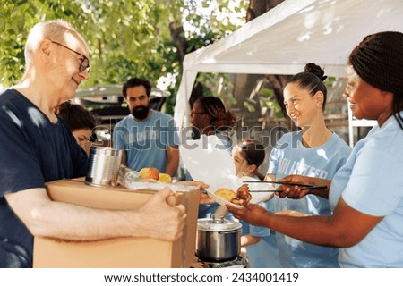 Charity wokers happily provide food donations to the poor, including homeless individuals and seniors. Hunger relief team distribute meal boxes and packages of canned goods with genuine smiles. Royalty-Free Stock Photo #2434001419