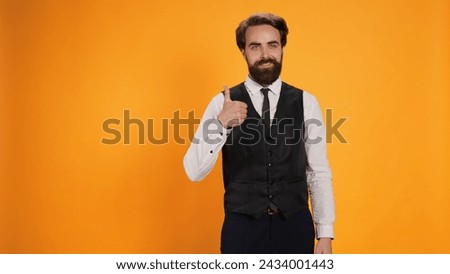 Trendy valet raises thumbs up gesture in studio to symbolize satisfaction and to indicate acceptance. Professional catering providers giving their seal of approbation on camera.