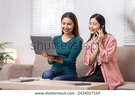 Two Asian women communicate with their friends and classmates via video link using a laptop and smartphone in the living room. Friends, friendship, happy time together