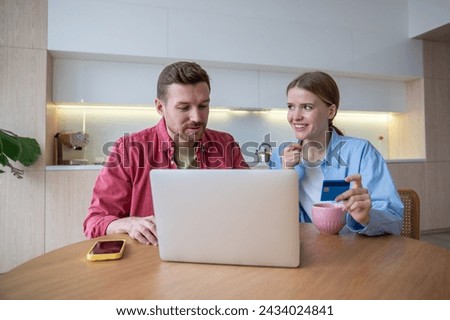 Happy excited family using laptop and bank card together, sitting at wooden table kitchen. Attractive woman smiling man feel euphoric from online shopping and book tickets. Joy shopping with discounts